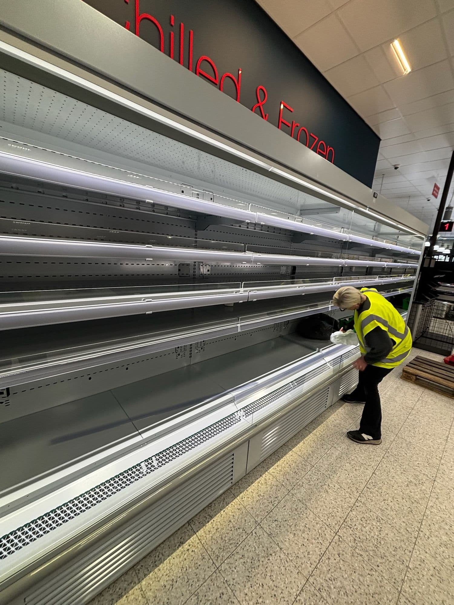 Team member in hi-vis cleaning a long refrigerated display in a new store