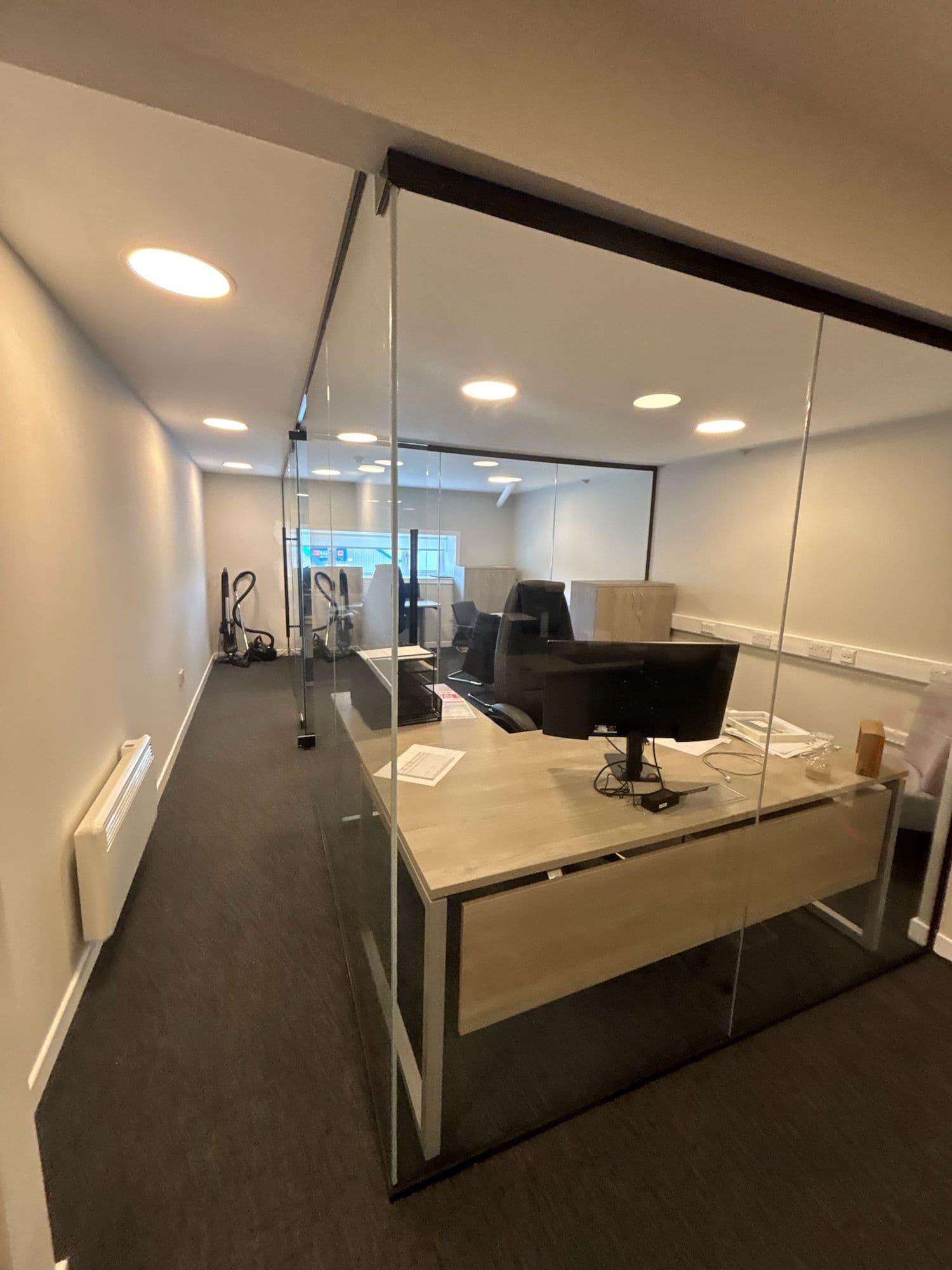 Glass-walled private office with a timber desk and dark carpet